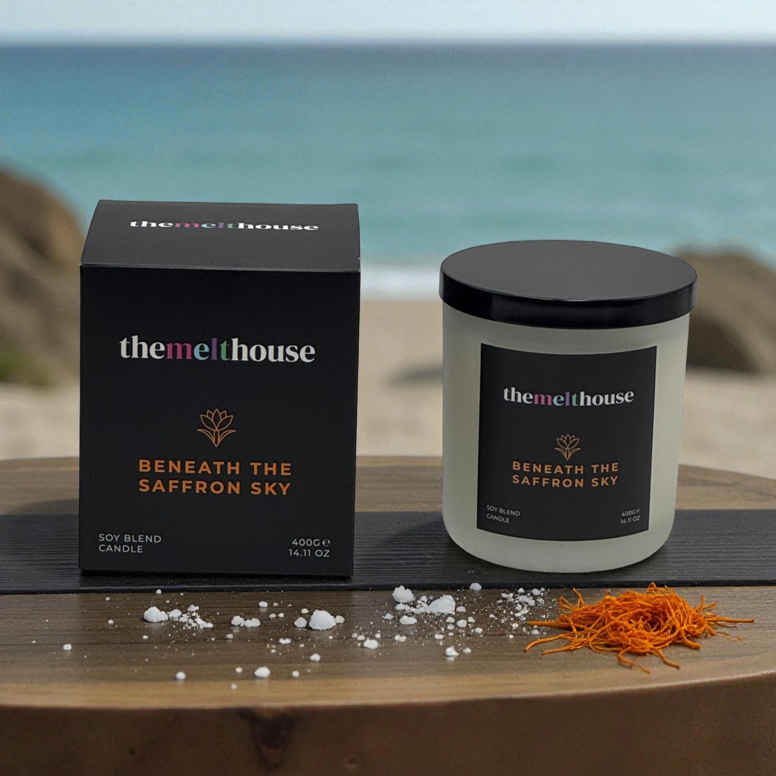 Beneath the Saffron Sky The Melthouse candle and packaging with saffron elements on a wooden surface by the ocean.