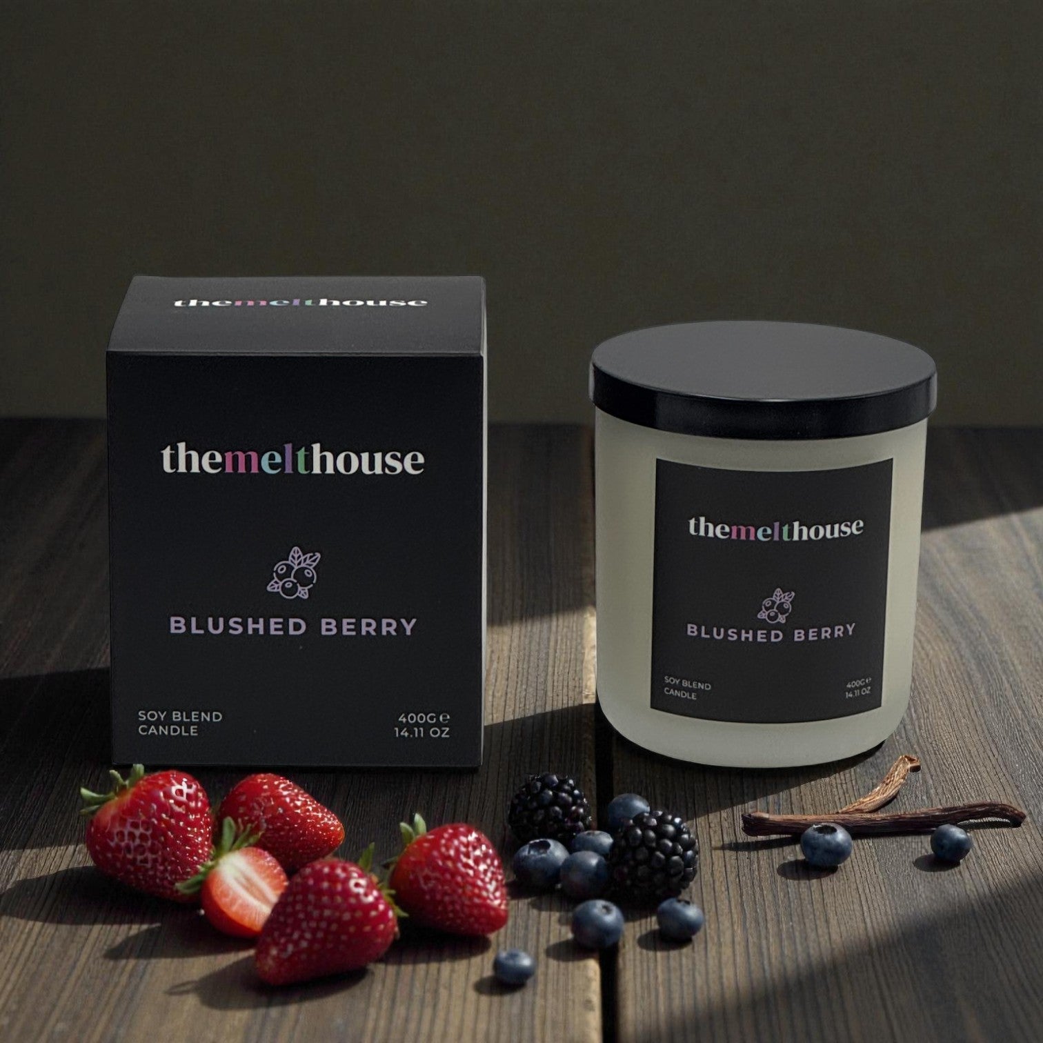 The Melthouse Blushed Berry candle and packaging on a wooden surface with berries and vanilla beans.