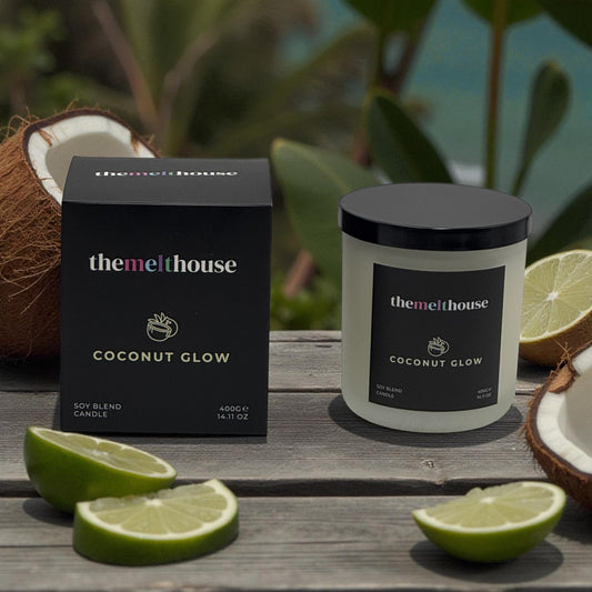 Themelthouse Coconut Glow candle and packaging on a wooden surface with limes and coconuts.
