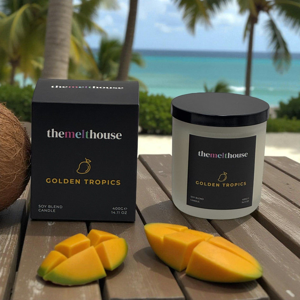 The Melthouse Golden Tropics candle and packaging on a wooden table with a beach background